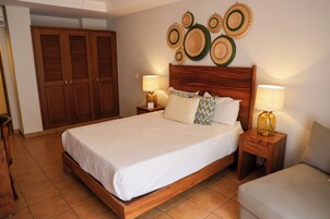 Un dormitorio con una cama de madera, dos mesitas de noche con lámparas, un armario y un panel decorativo con platos tejidos.