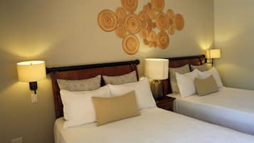 A hotel room with two beds, each with white bedding and multiple pillows. There are wall-mounted lamps on either side of the beds.