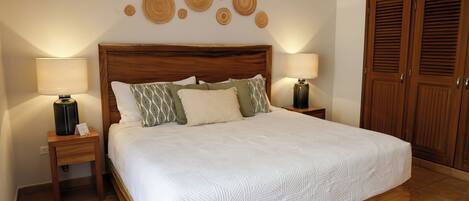 A bedroom with a large bed, two bedside tables, a wooden wardrobe, and wall decor.