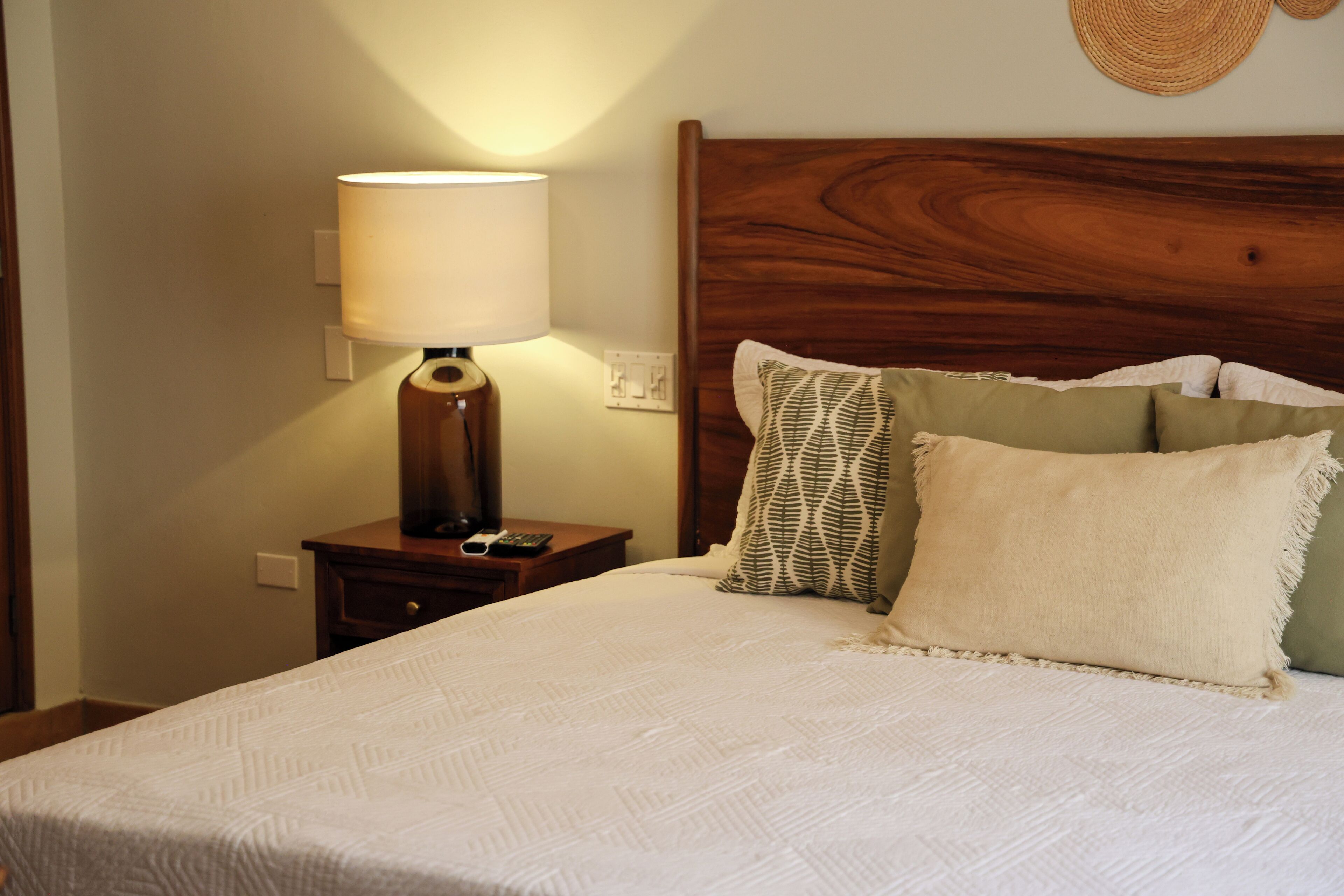 A neatly made bed with a wooden headboard, a bedside lamp, and a small nightstand with a remote control.