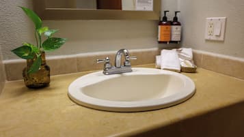 Un lavabo dans la salle de bain, avec un miroir au-dessus, une plante sur la gauche et des articles de toilette accrochés au mur.