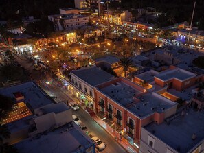 Vue aérienne d'un quartier urbain animé la nuit, avec des rues et des bâtiments illuminés.