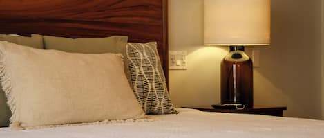 Een netjes opgemaakt bed met een houten hoofdbord, een bedlampje en twee kussens.