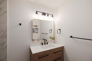 A bathroom with a white vanity, a large mirror, and a light fixture above the mirror. - Luxury Waterfront Cottage with Panoramic Waterway Views (Wilmington)