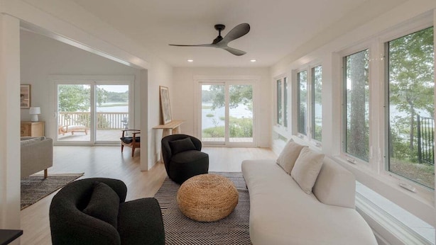 A spacious living room with a large window, a ceiling fan, and a view of the outdoors. - Luxury Waterfront Cottage with Panoramic Waterway Views (Wilmington)