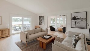 A spacious living room with a large sofa, a coffee table, and a view of the outdoors through large windows. - Luxury Waterfront Cottage with Panoramic Waterway Views (Wilmington)