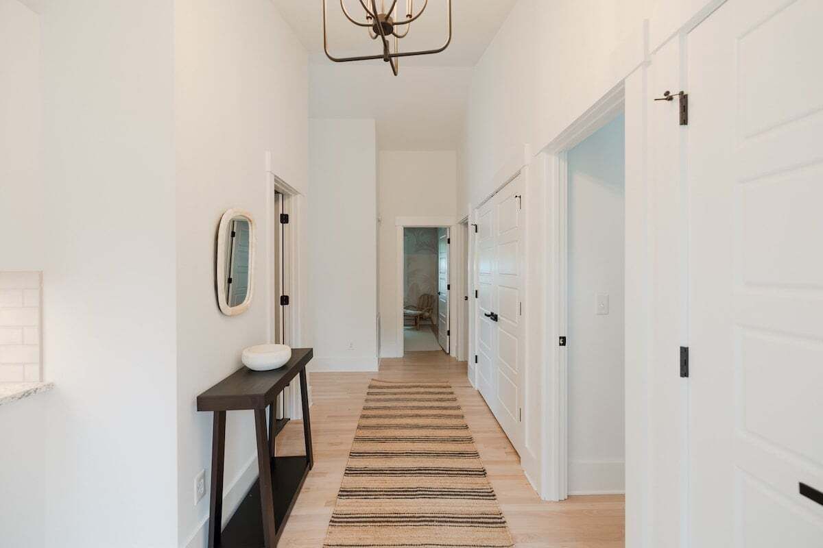 A hallway with a wooden floor, a striped rug, a round mirror, and a white door.