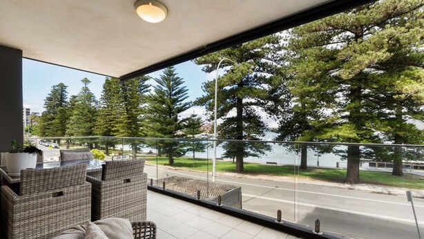 A balcony with wicker furniture, a view of a road, and trees.