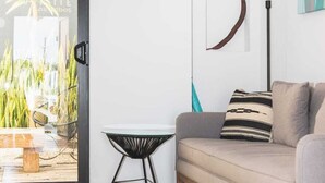 Ein modernes Wohnzimmer mit einem grauen Sofa, einem gewebten Teppich, einem kleinen schwarzen Tisch und Blick auf einen Garten durch eine Glastür.