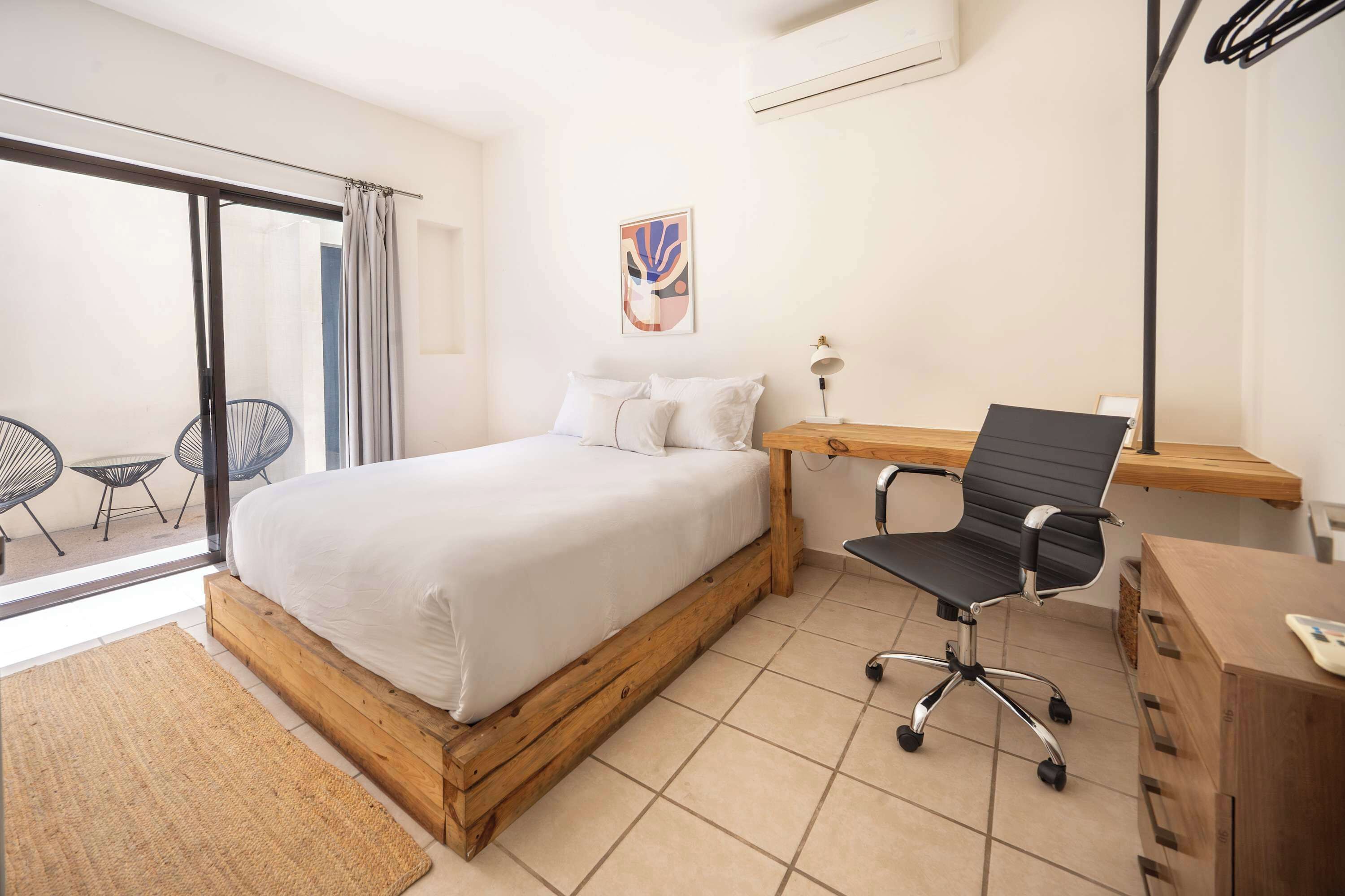 A bedroom with a bed, a desk, a chair, and a view of the outside.