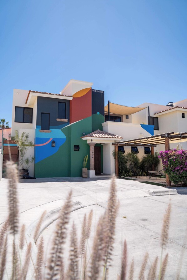 A modern house with a colorful exterior, a patio area with plants, and a pergola. - Casa Alonso | Spacious House with Private Courtyard in San Jose (San José del Cabo)