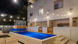 A swimming pool with a blue interior, surrounded by a white deck and outdoor furniture. - Beach Home | Steps to Sand | Pool & Jacuzzi Unit A (Bahía la Choya)