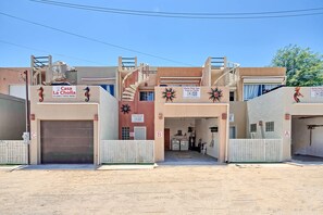 Ein mehrstöckiges Gebäude mit einer zentralen Treppe, mehreren Garagentoren und Schildern mit den Aufschriften 'Casa La Cholla' und 'Rocky Point Tom'.