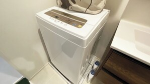 Une petite machine à laver blanche, dotée d’un panneau de commande, est installée dans une petite salle de bain carrelée.