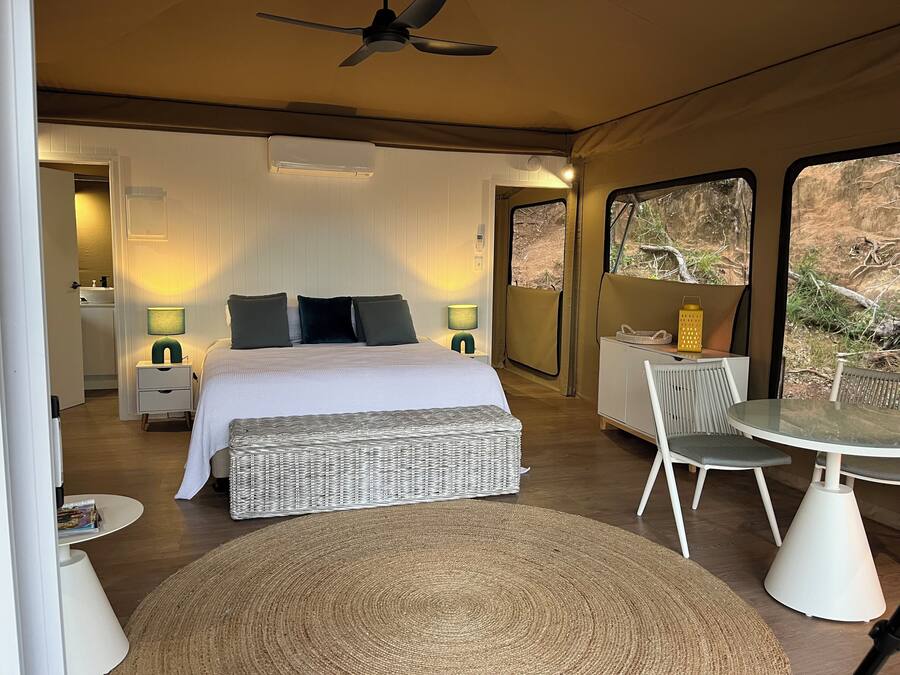 Una camera da letto con un letto, due abat-jour, un tavolino e una sedia. Si vede una finestra con vista sull'esterno.