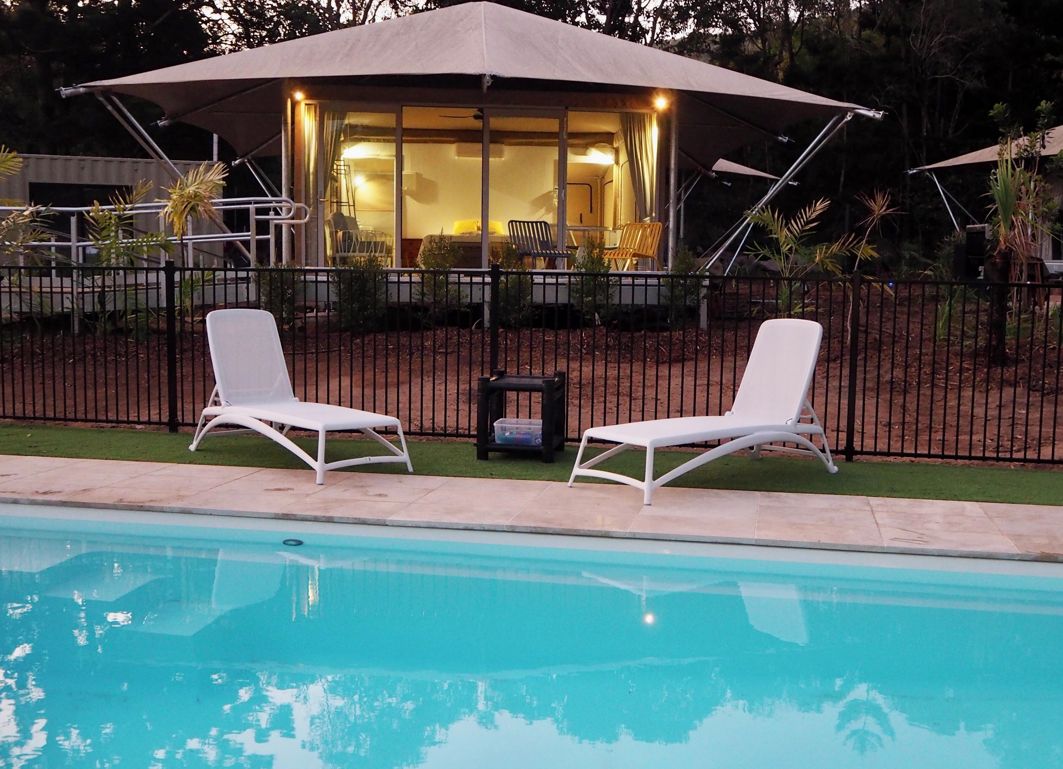 A pool area with two white lounge chairs and a covered seating area with a table and chairs.