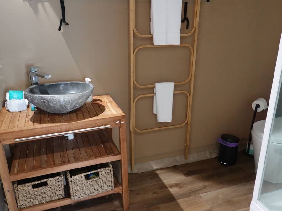 Een badkamer met een stenen wastafel, een houten wastafelmeubel, rieten manden, een handdoekhouder en een douchecabine met glazen wanden.