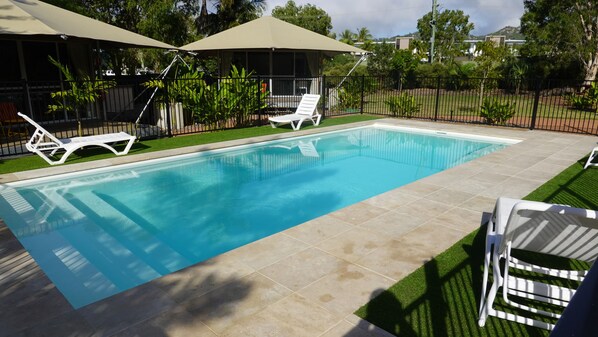 A rectangular swimming pool with tiled edges, surrounded by a grassy area and a black metal fence. - Magnetic Glamping (Nelly Bay)