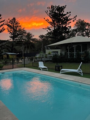 A swimming pool with two white lounge chairs, surrounded by a fence and trees. - Magnetic Glamping (Nelly Bay)