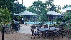 An outdoor patio area with a pool, umbrellas, and outdoor furniture. - Magnetic Glamping (Nelly Bay)