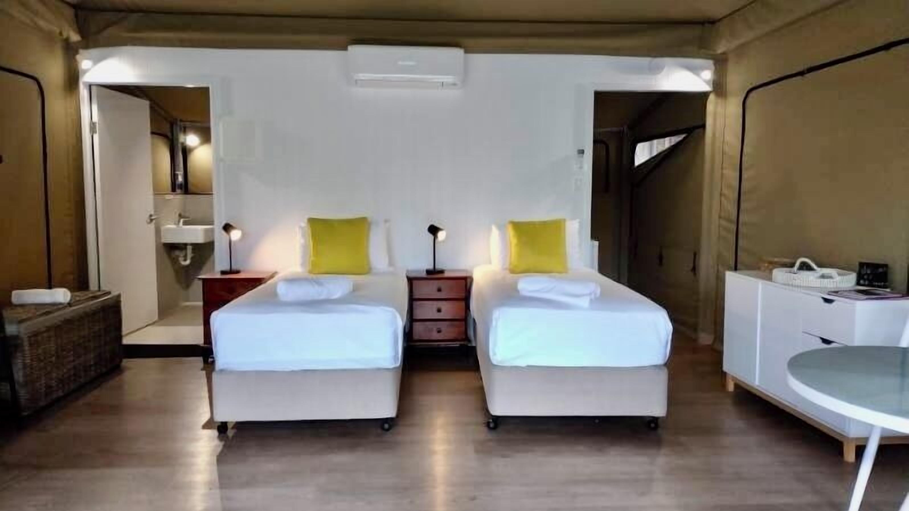 A room with two beds, a small desk, a chair, a sink, and a mirror.