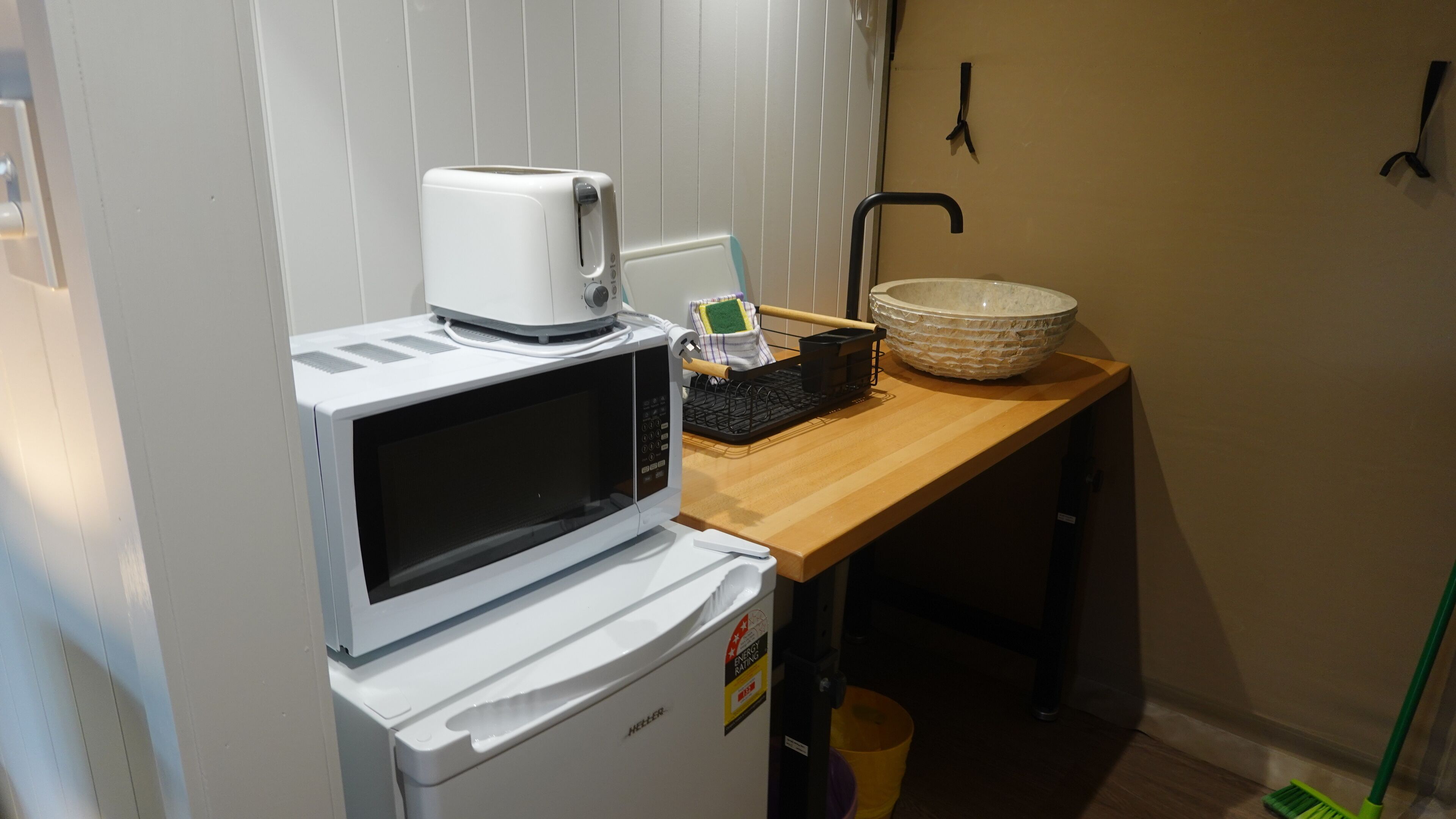 A compact kitchenette with a microwave, toaster, and a sink with a bowl.