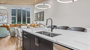 Una cocina moderna con una isla central, un comedor con sillas, un sofá y un ventanal grande.