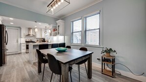 A modern kitchen with white cabinets, a wooden dining table, and a large window with blinds. - Chic & Spacious Bi-Level Bucktown Condo - Sleeps 8 (Chicago)