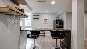 A modern kitchen with a marble island, two black bar stools, a black refrigerator, and a window with natural light. - Chic & Spacious Bi-Level Bucktown Condo - Sleeps 8 (Chicago)