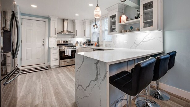 A modern kitchen with white cabinetry, a marble island, and black bar stools. - Chic & Spacious Bi-Level Bucktown Condo - Sleeps 8 (Chicago)