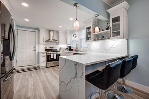 A modern kitchen with white cabinetry, a marble island, and black bar stools. - Chic & Spacious Bi-Level Bucktown Condo - Sleeps 8 (Chicago)