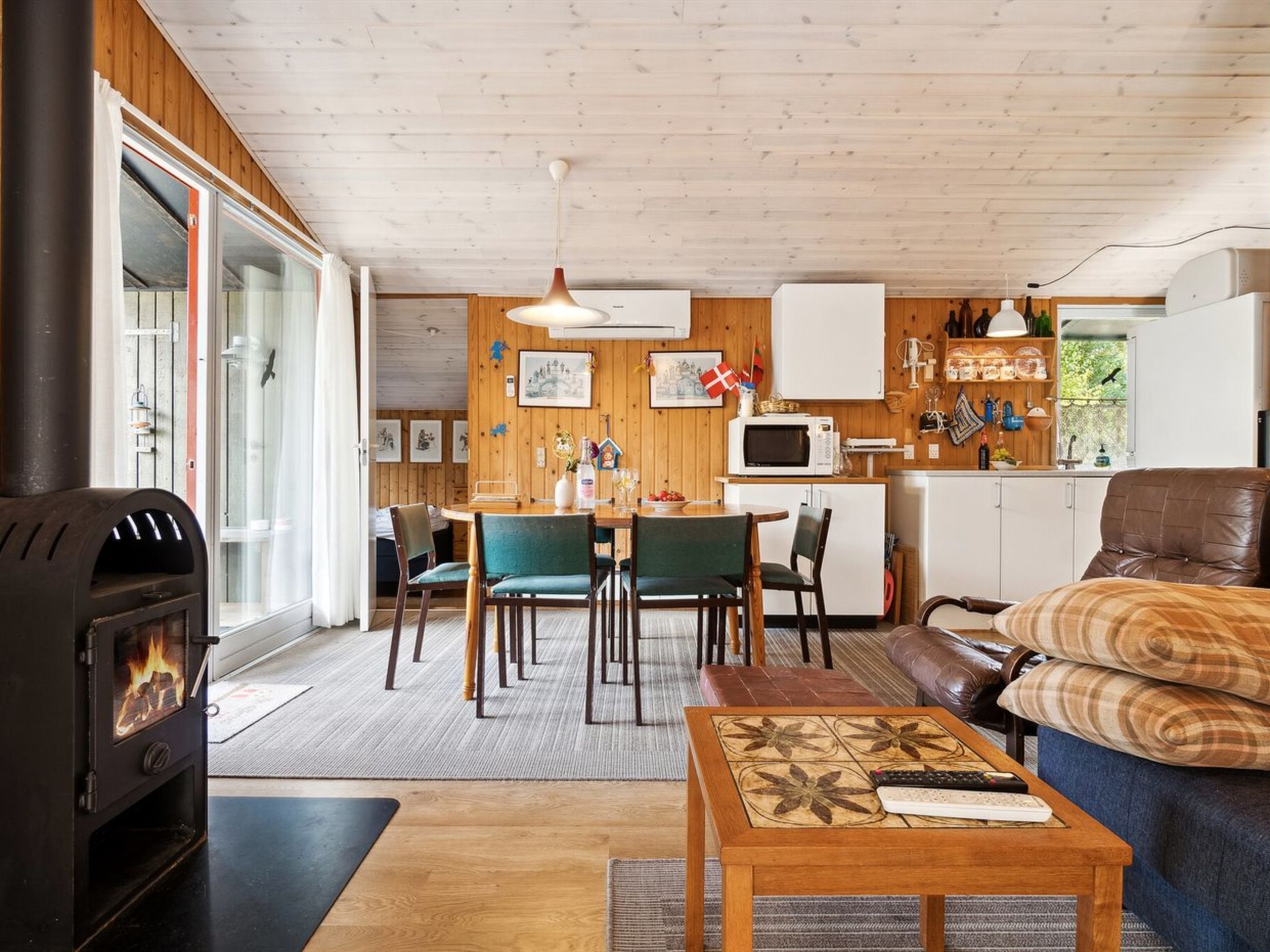 Un salon chaleureux avec une cheminée, un coin repas et une cuisine aux murs en bois et aux armoires blanches.