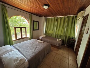 A room with two beds, a wooden ceiling, a window with green curtains, and a small table with a plant. - Refugio de Playa en Guanacaste Costa Rica (Santa Cruz)