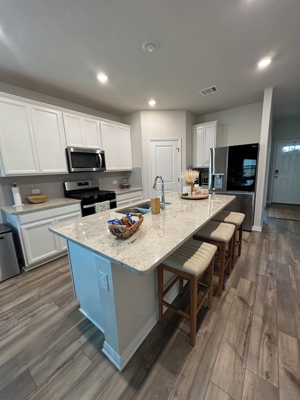 A modern kitchen with white cabinetry, a granite countertop, stainless steel appliances, and a wooden floor.