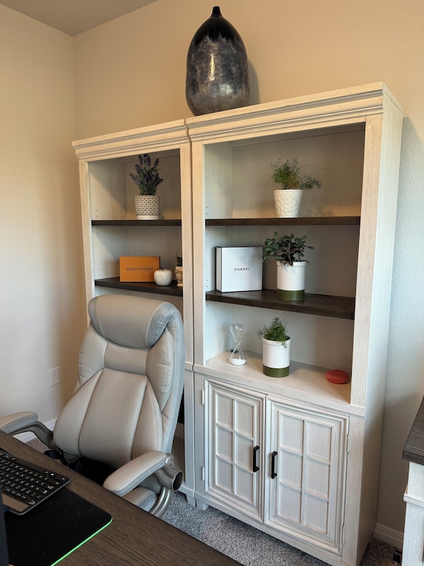 A room with a white cabinet containing a Louis Vuitton box, a Chanel box, and potted plants.
