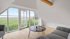 A spacious loft bedroom with large windows, a wooden ceiling beam, and a round table with a newspaper. - Nice home in Janderup Vestj with sauna (Janderup Vestj)