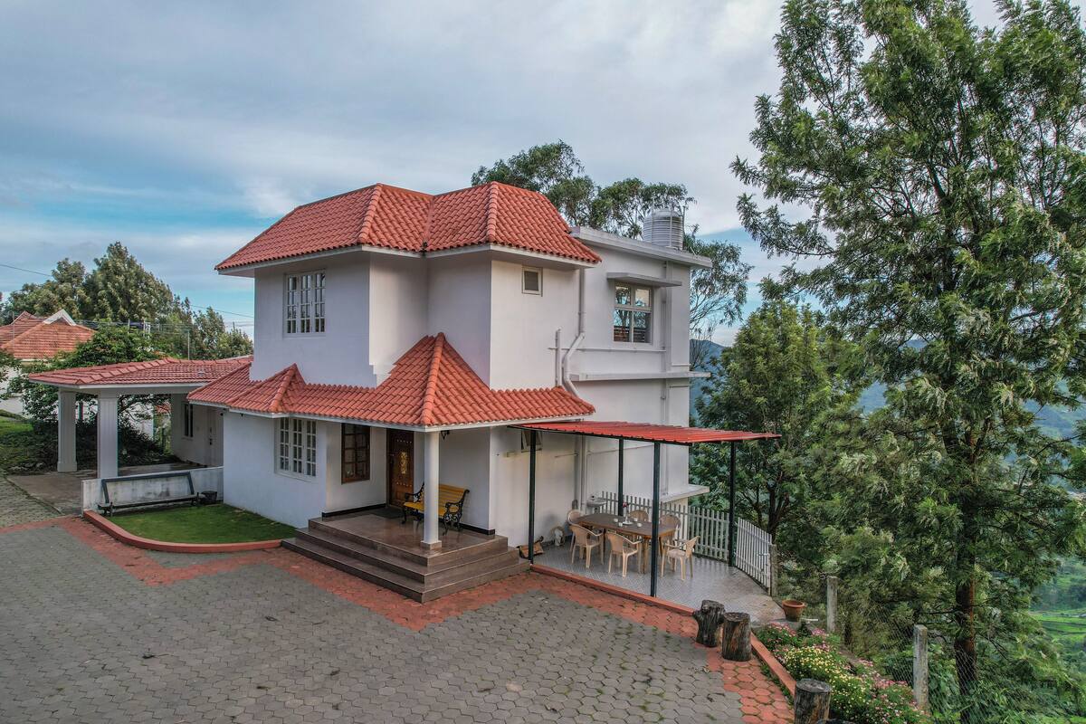 A two-story house with a red-tiled roof, a covered porch, and a view of a lush green landscape.