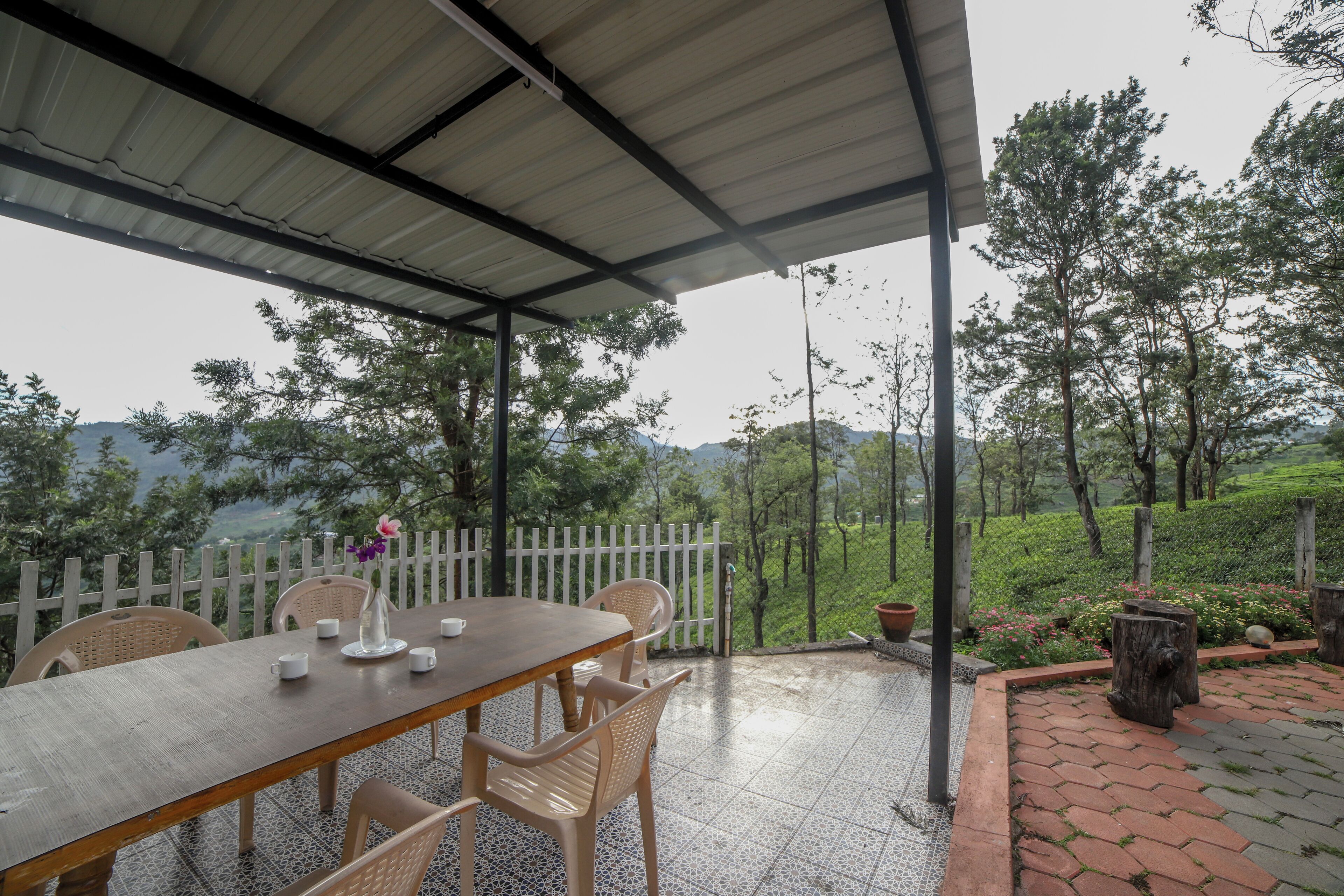 A covered patio with a table and chairs, overlooking a lush garden and distant hills.