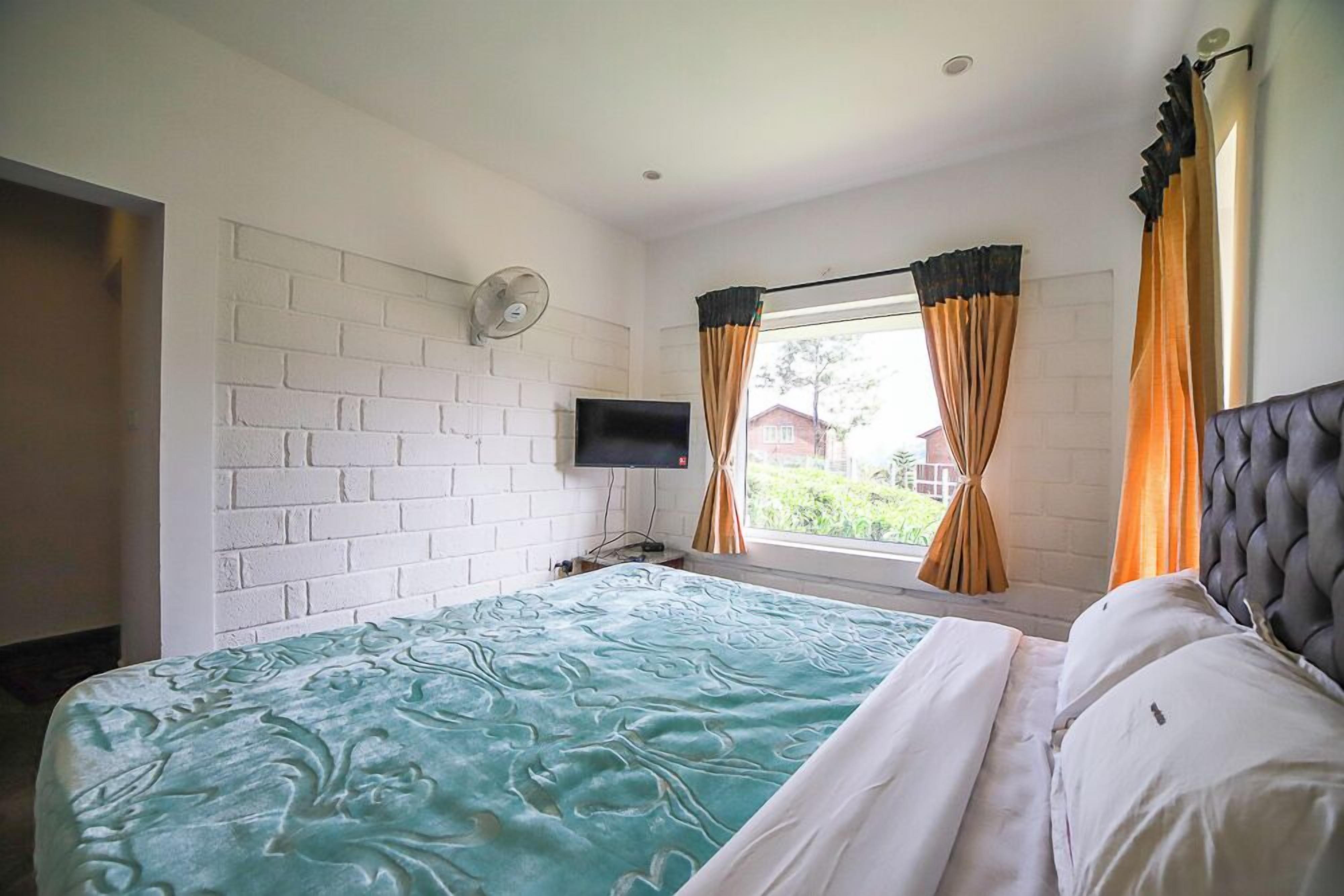 A bedroom with a bed, a flat-screen TV, a window with curtains, and a brick wall.