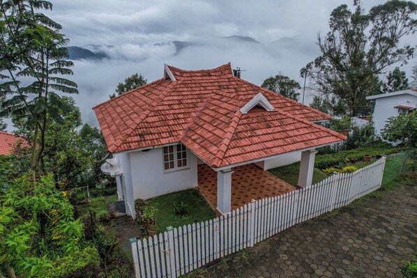 A house with a red tiled roof, surrounded by lush greenery and a white picket fence. - Samrakshitha - The Villa (Kotagiri)