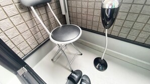 A small, compact bathroom with a shower chair, a handheld showerhead, and a pair of slippers on the floor. - Skytree & Asakusa in front! Newly built clean apt! (墨田区)