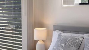 Un lit bien fait, avec une serviette enroulée, une lampe de chevet et une fenêtre avec des stores.