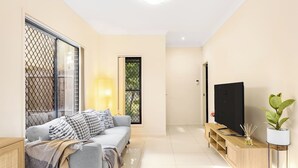 Un salon moderne avec un ensemble de canapés, un téléviseur posé sur un meuble en bois et une plante en pot.