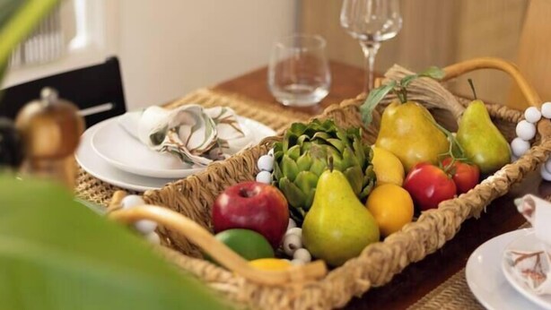Une table à manger avec un panier de fruits, des assiettes et une bougie.