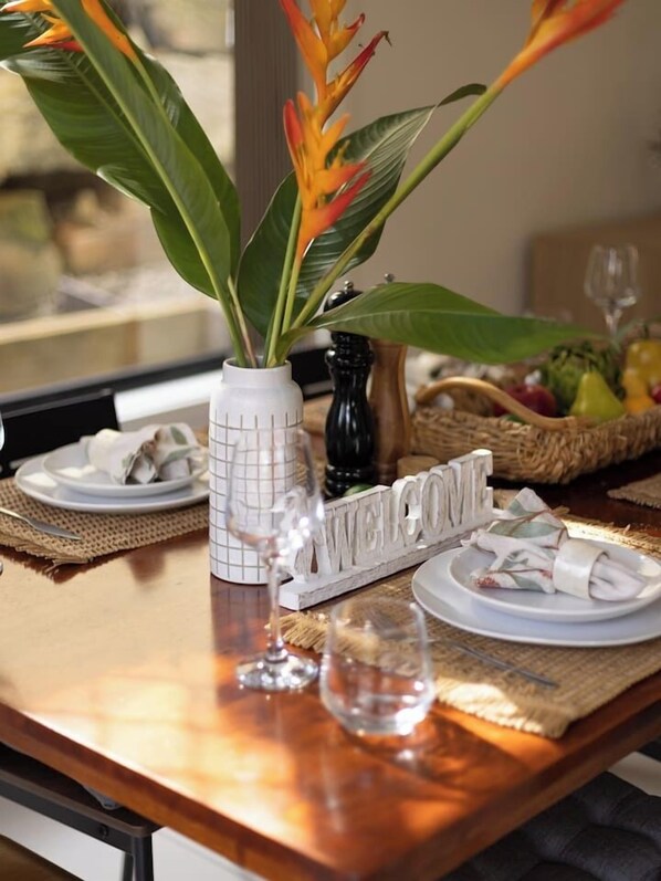 A dining table with a 'WELCOME' sign, a vase with a plant, and a basket of fruit.