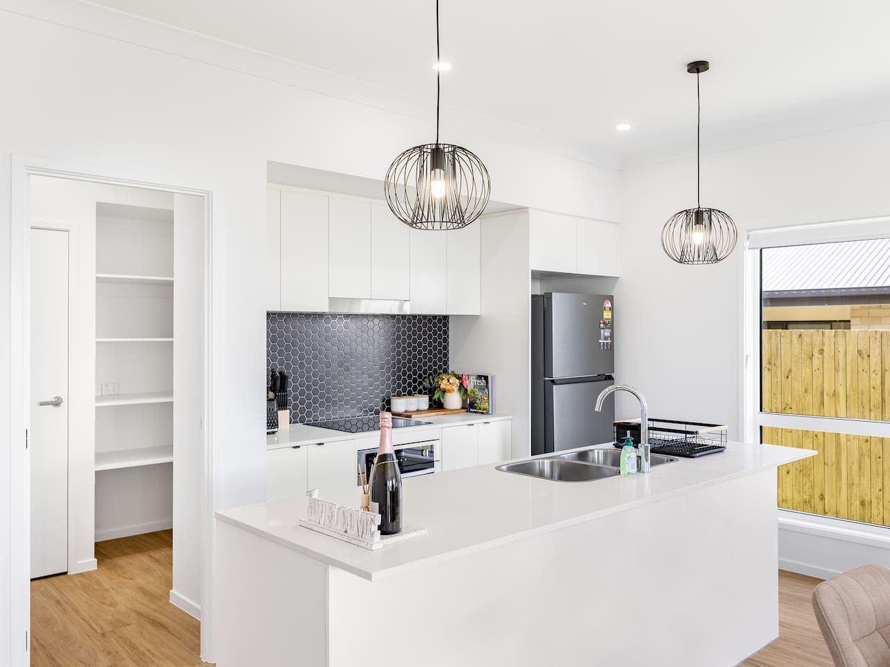 Une cuisine moderne avec des meubles blancs, un îlot central, un four encastré et un réfrigérateur en acier inoxydable.