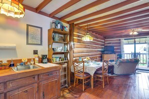 A rustic cabin interior with a wooden dining table, chairs, a sofa, and a kitchen area with a sink and shelves. - Cozy Luray Cabin w/ Views: Near Hiking Trails! (Luray)
