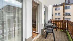 Un balcon avec une table et des chaises, une porte-fenêtre coulissante et une vue sur un immeuble doté de nombreuses fenêtres.