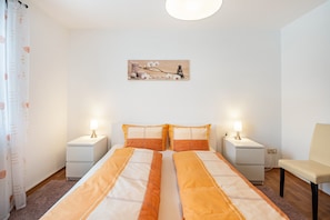 Une chambre avec deux lits, deux tables de chevet, une chaise et un tableau accroché au mur.