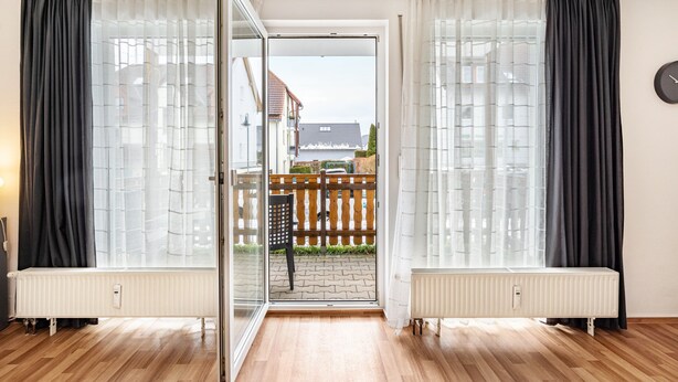 Une pièce dotée d’une porte-fenêtre coulissante donnant sur une terrasse extérieure, d’un radiateur et d’une horloge murale.